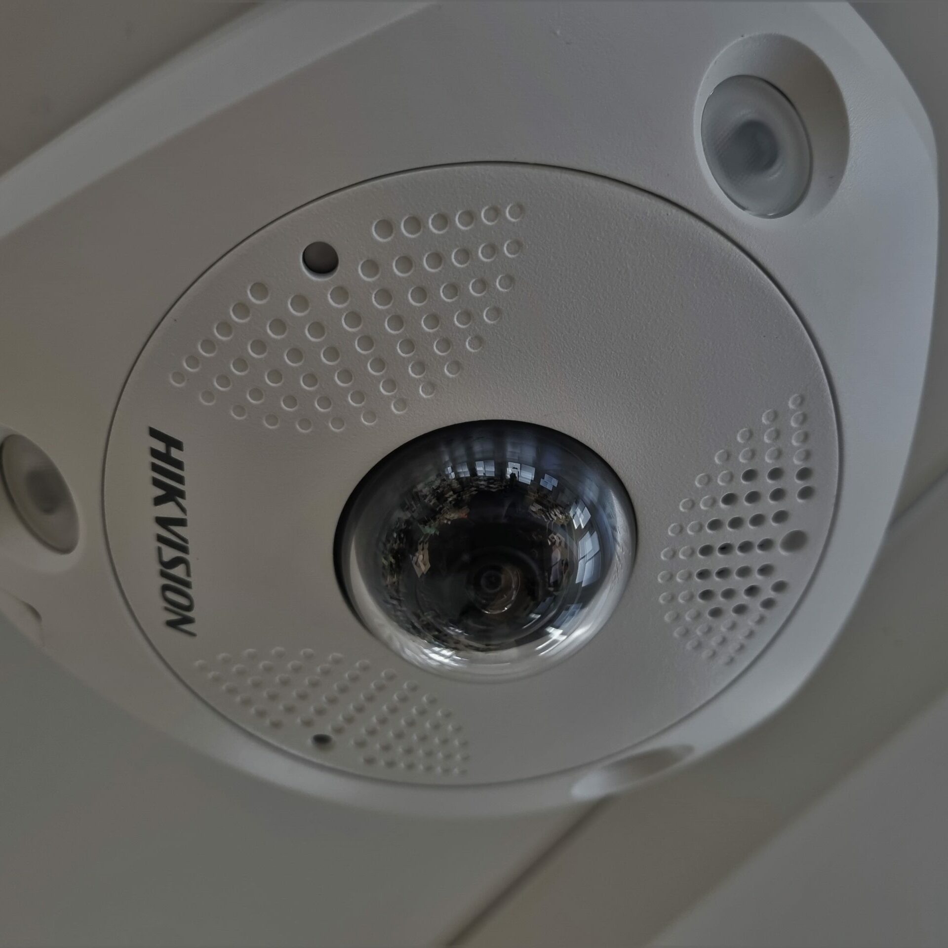 Image of a white Hikvision CCTV camera mounted to the ceiling that can record audio/sound as part of a security system.