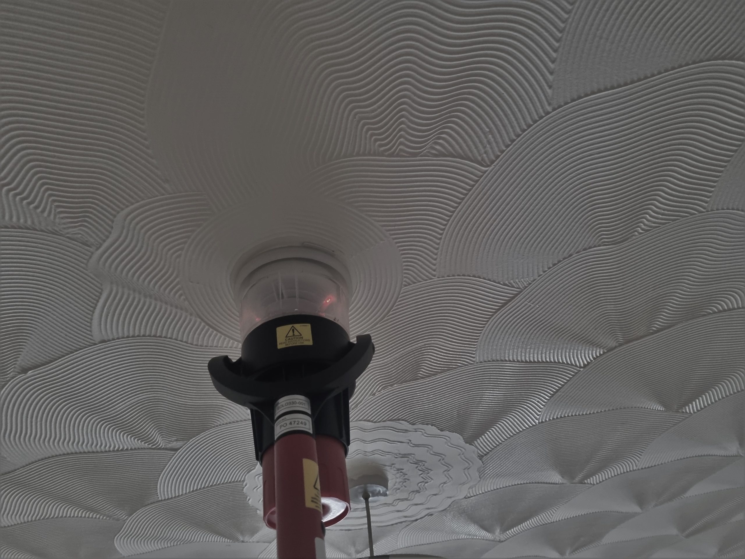 Engineer testing a device smoke detector on a celing as part of a fire alarm maintenance