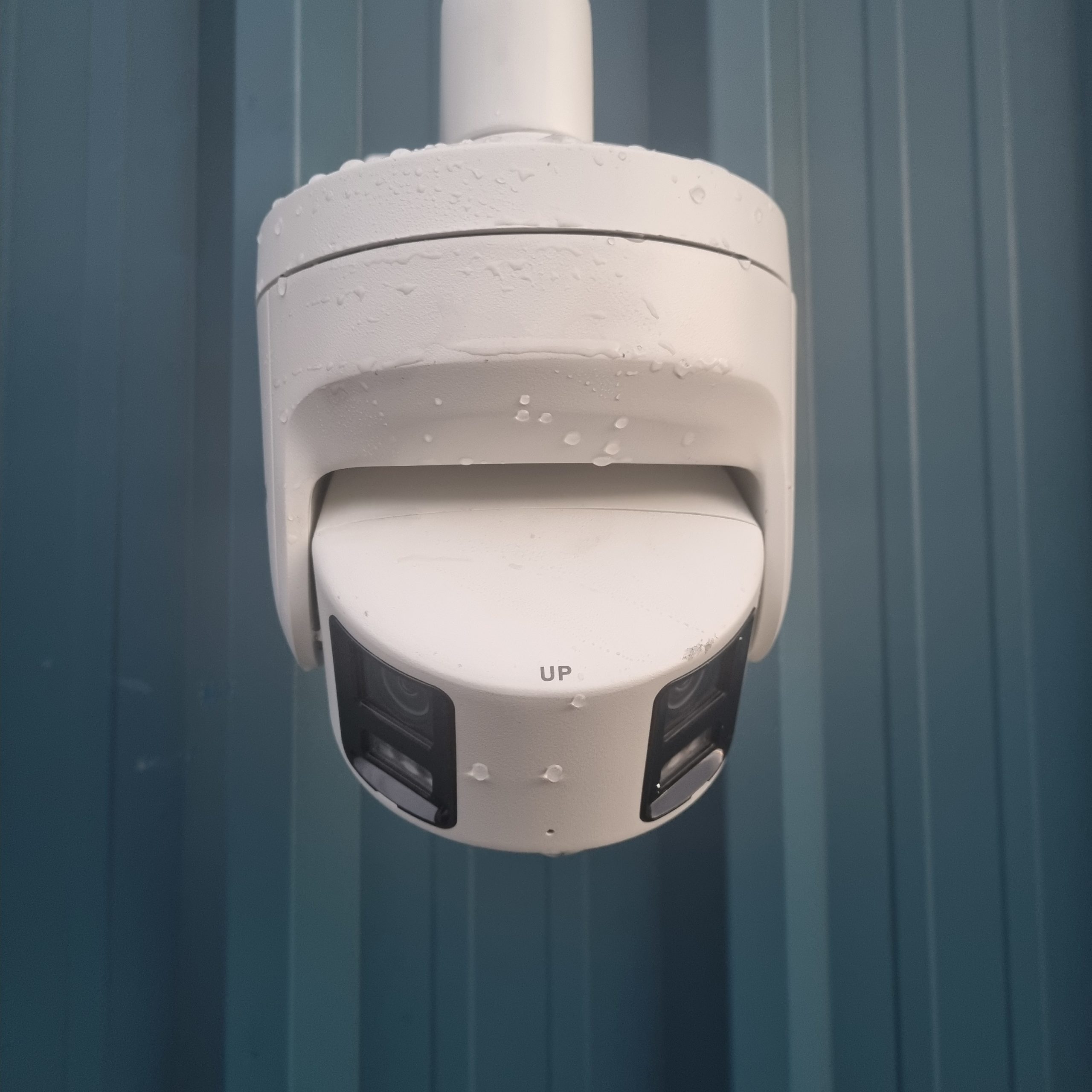 A white CCTV camera on a blue metal wall