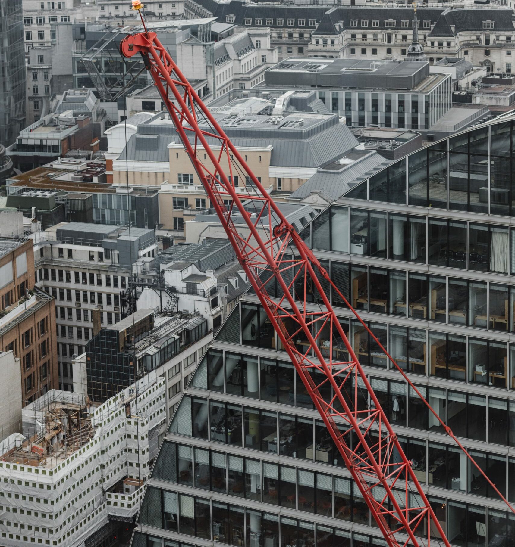 An image of a red crane in a construction site in the UK with buildings in the background