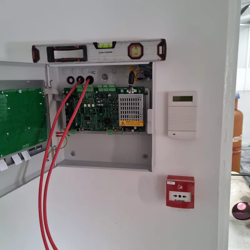 A image of a Fire alarm installation being carried out, consisting of a control panel that is open with red cables coming out.