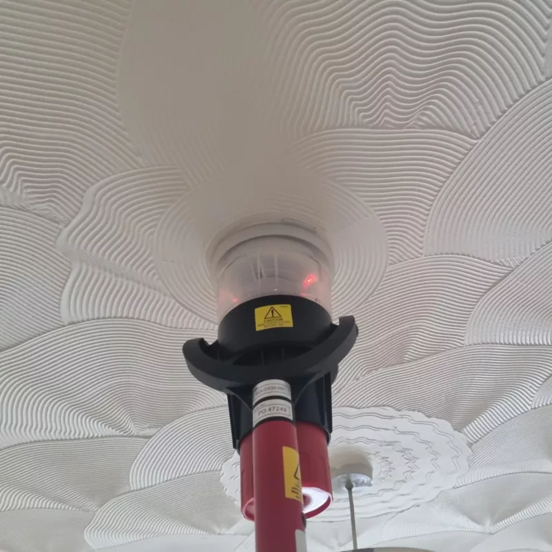 Engineer testing a device smoke detector on a celing as part of a fire alarm maintenance