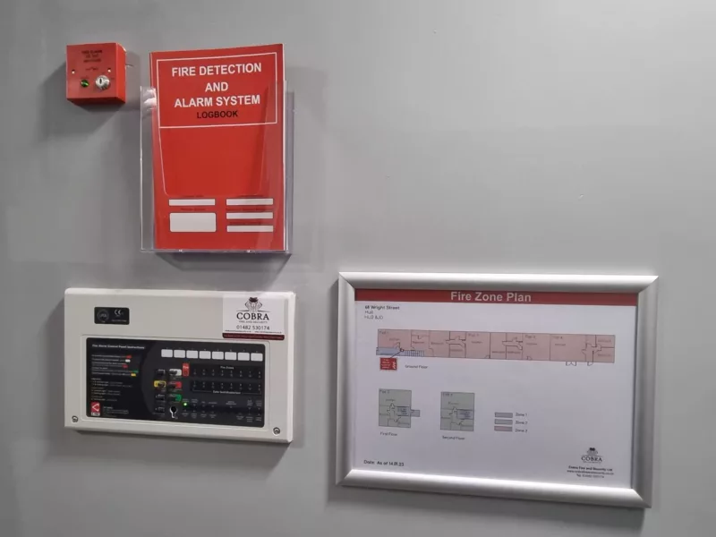 Fire Alarm panel mounted on a wall alongside a zone plan and fire alarm log book