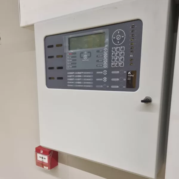 Advanced fire alarl control panel mounted on a wall above a manual call point