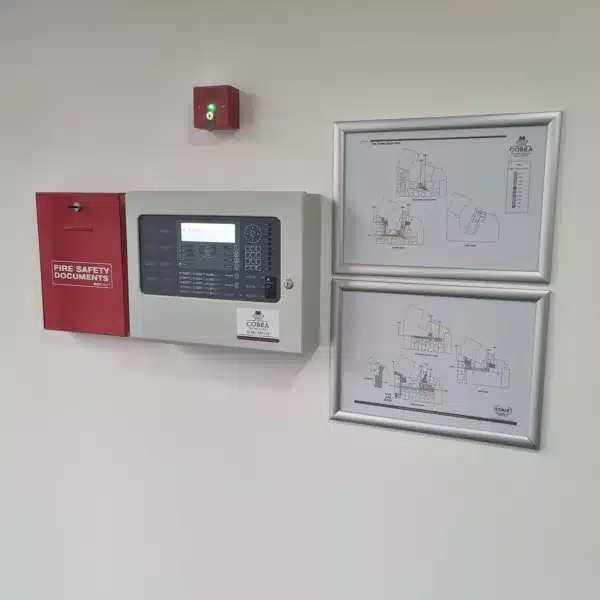 Fire Alarm installed on a white wall. Next to two fire alarm zone plans, document box and a key switch for the fire alarm