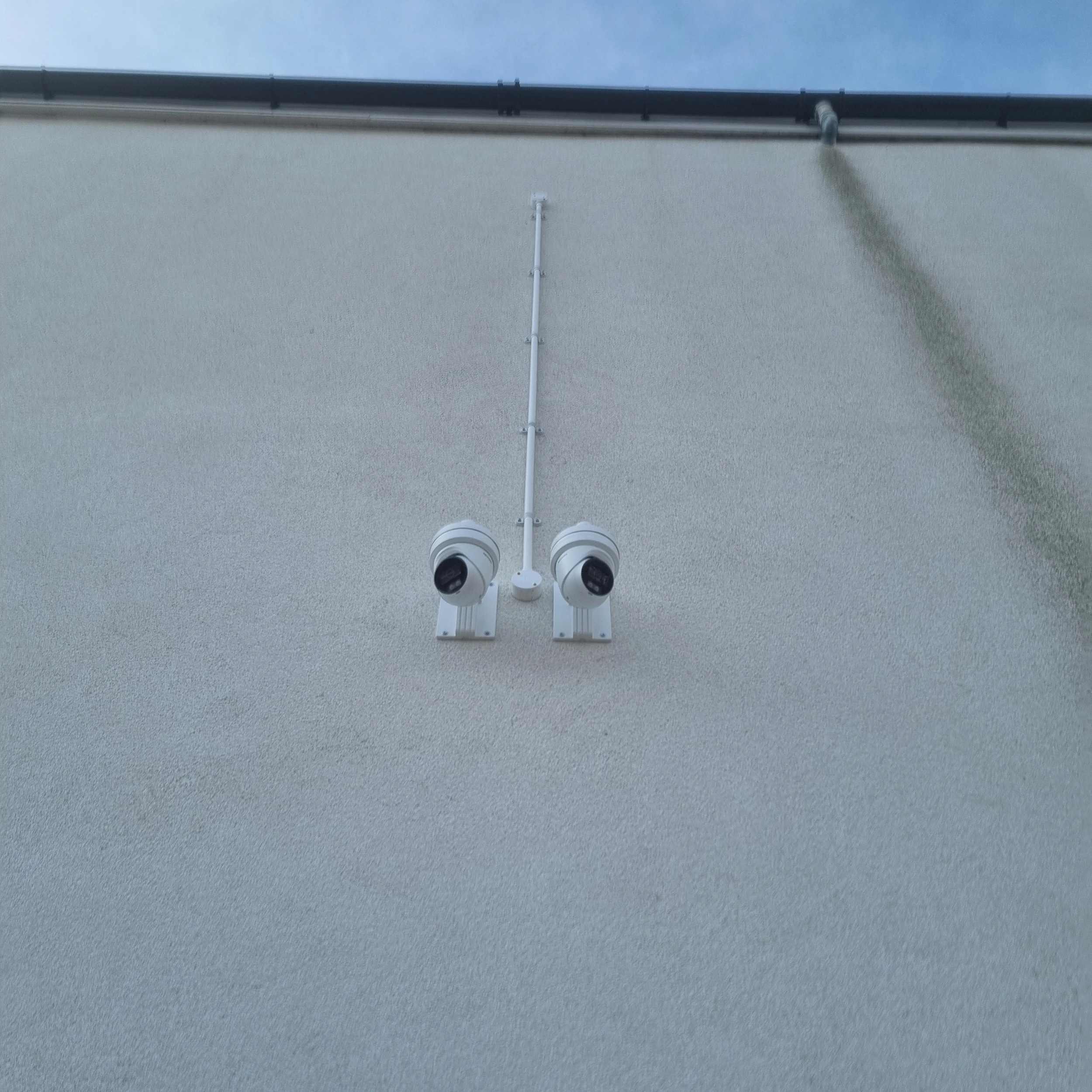 Two cameras on a white wall looking in the opposite direction.