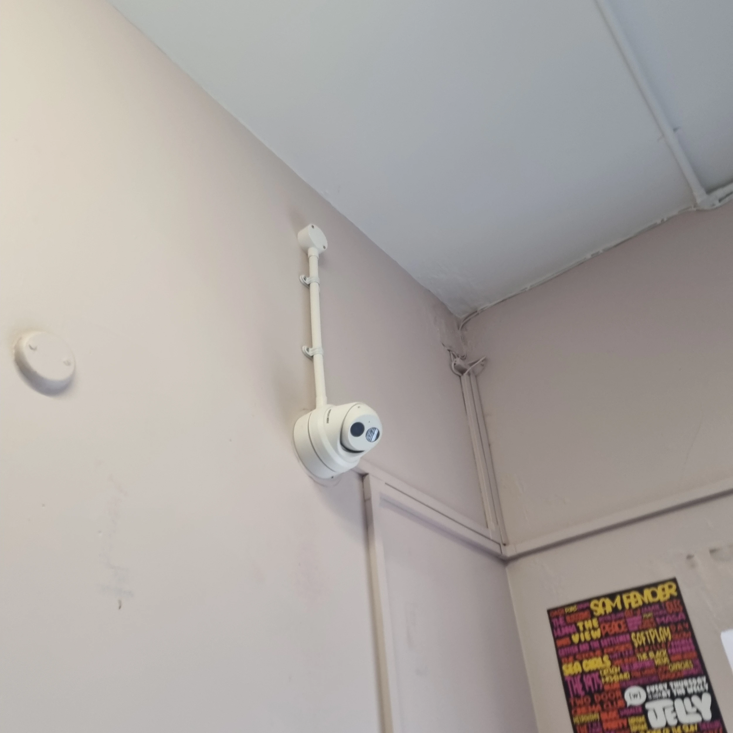 A white CCTV camera mounted high on a wall within a building.