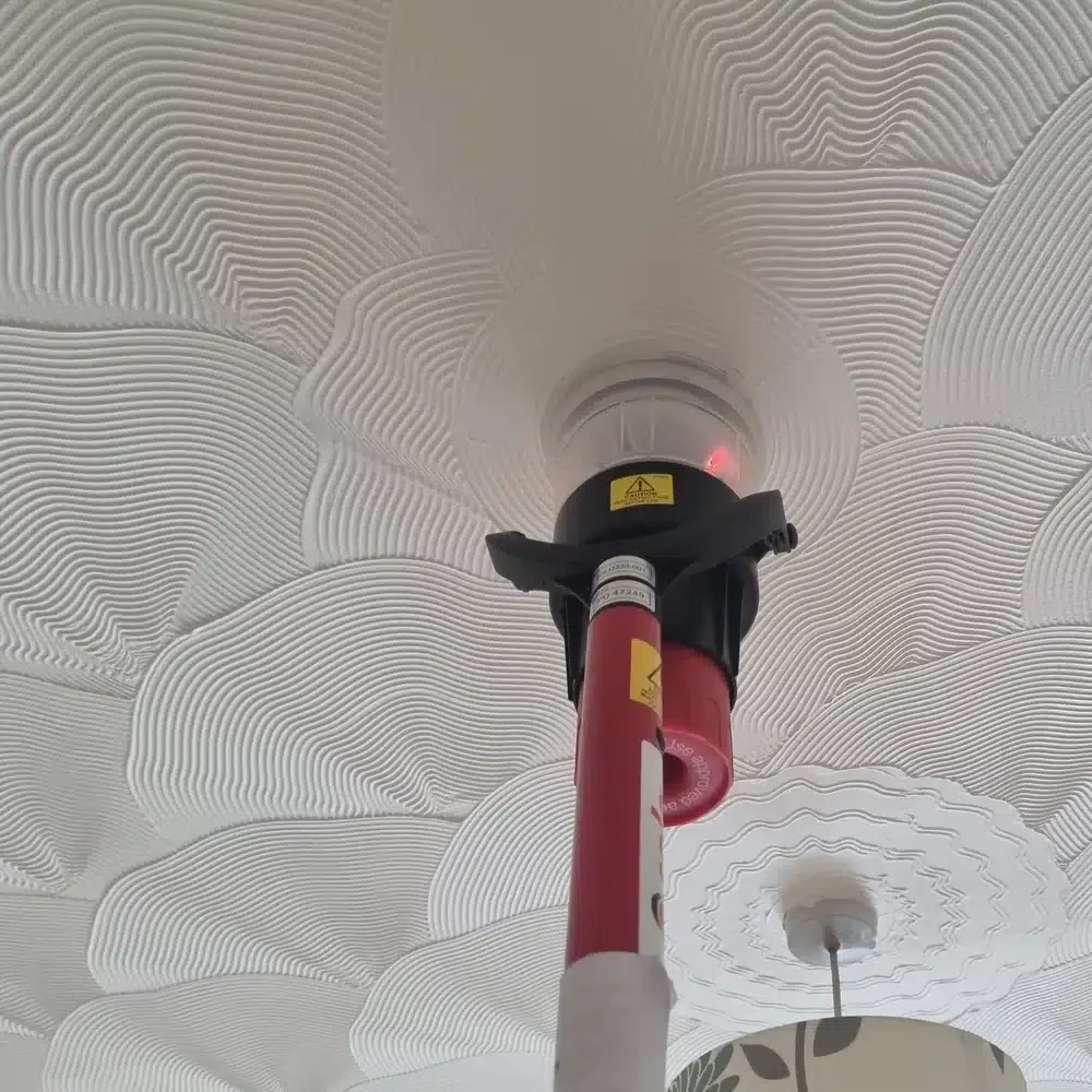 Engineer testing a ceiling mounted smoke detector using a Solo test pole during fire alarm maintenance.