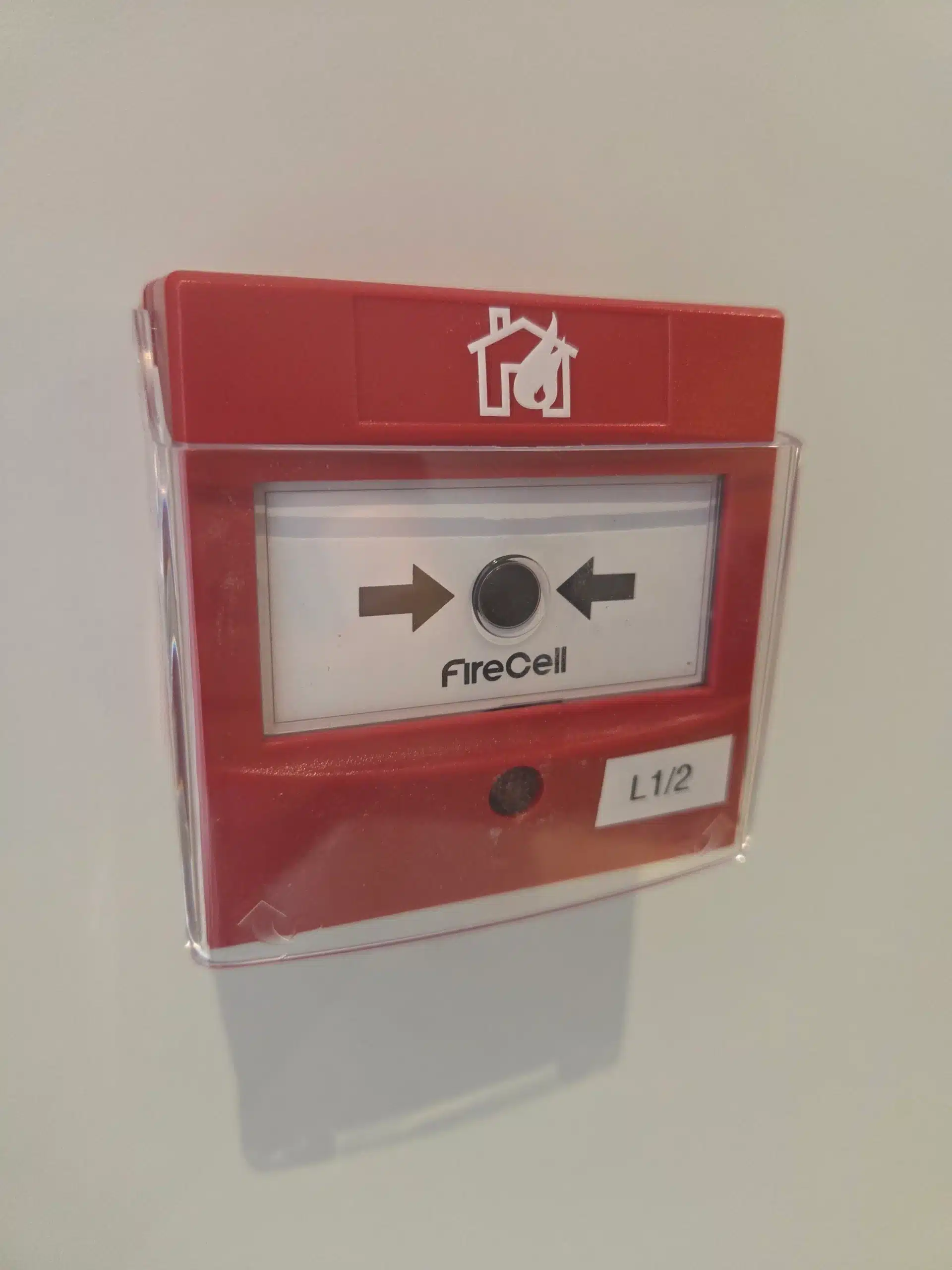 FireCell wireless manual call point with protective cover installed as part of a fire alarm system.